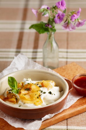 Close-up of dumplings with sour cream and baked apples in brown dish on wooden cutting boardの写真素材