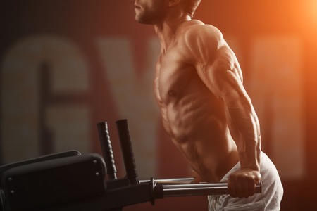 Strong muscular bodybuilder doing exercise on bars in the gym