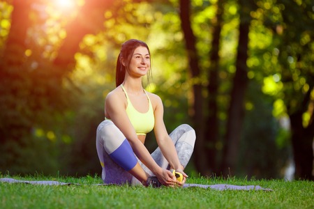 Young smiling woman doing fitness exercises in the park on the green grass. Fitness training in the sunlight.の写真素材