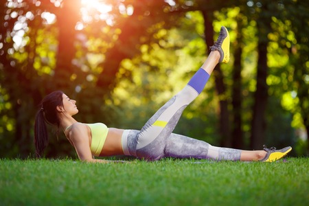 Young smiling woman doing fitness exercises in the park on the green grass. Fitness training in the sunlight.の写真素材