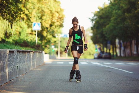 Beautiful, athletic, young woman in black sportswear, to roller skate on the road. Cheerful girl on roller skates in the rays of the setting sun. Active lifestyleの写真素材