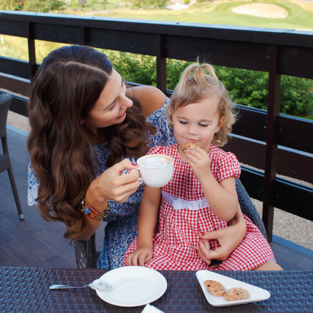 Happy mom and daughter eating ice cream and drinking coffee outdoors. Family sitting at a table in the outdoor cafe and eating ice cream.の写真素材