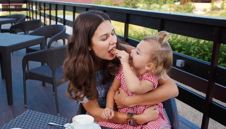 Happy mom and daughter eating ice cream and drinking coffee outdoors. Family sitting at a table in the outdoor cafe and eating ice cream.の写真素材