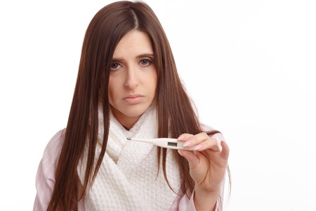 Young sick woman in scarf and pajamas looking at thermometer. Sick girl with a thermometer on a white background, isolate, flu, coldsの写真素材