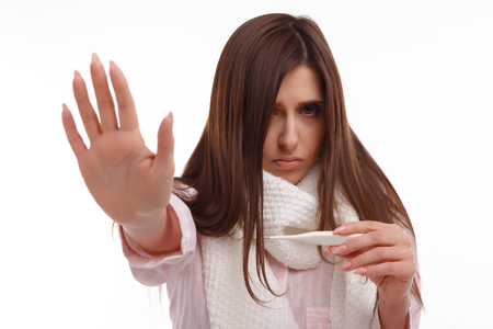 Young ill woman in a scarf and looking at the thermometer shows STOP. Sick girl with a thermometer on a white background, isolate, flu, coldsの写真素材
