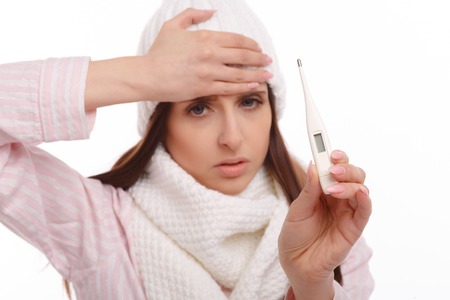 Young sick woman in scarf and pajamas looking at thermometer. Sick girl with a thermometer on a white background, isolate, flu, coldsの写真素材