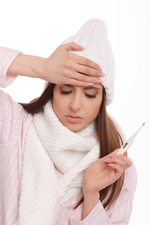 Young sick woman in scarf and pajamas looking at thermometer. Sick girl with a thermometer on a white background, isolate, flu, coldsの写真素材