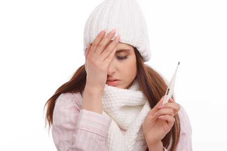 Young sick woman in scarf and pajamas looking at thermometer. Sick girl with a thermometer on a white background, isolate, flu, coldsの写真素材