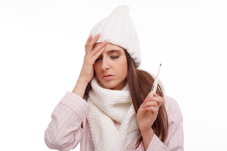 Young sick woman in scarf and pajamas looking at thermometer. Sick girl with a thermometer on a white background, isolate, flu, coldsの写真素材
