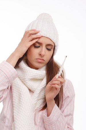 Young sick woman in scarf and pajamas looking at thermometer. Sick girl with a thermometer on a white background, isolate, flu, coldsの写真素材