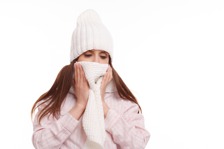 Young woman sick and closed with a scarf on white background. Sneezing into Tissue.の写真素材
