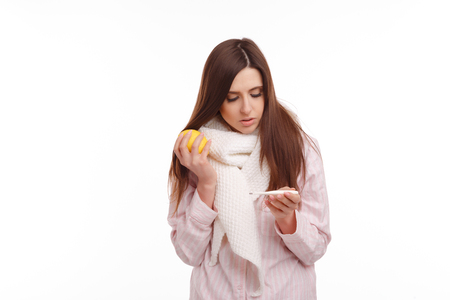 A sick young woman looking at the thermometer and holding a lemonの写真素材
