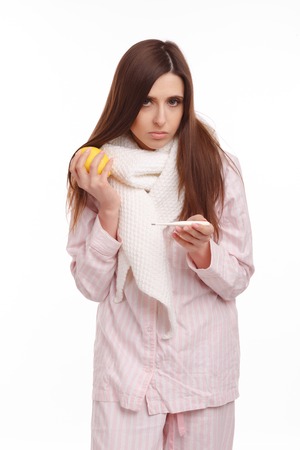 A sick young woman looking at the thermometer and holding a lemonの写真素材