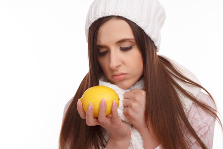Sick young woman in pajamas and scarf holding lemon on white background.の写真素材