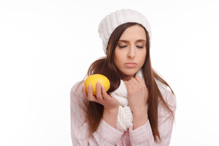 Sick young woman in pajamas and scarf holding lemon on white background.の写真素材