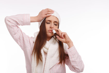 Sick young woman in pajamas scarf and hat use nasal spray. Woman applies nasal spray isolated. Sick Woman.Flu.Woman Caught Cold.の写真素材
