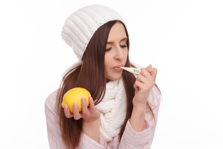 A sick young woman measures the temperature and holding a lemonの写真素材
