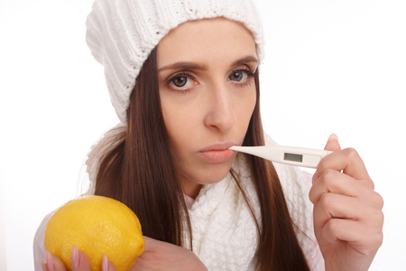 A sick young woman measures the temperature and holding a lemonの写真素材