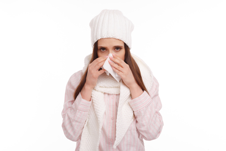 Sick young woman in pajamas scarf and hat coughing and blowing. Woman sick blowing nose isolated. Sick Woman. Flu. Woman Caught Coldの写真素材