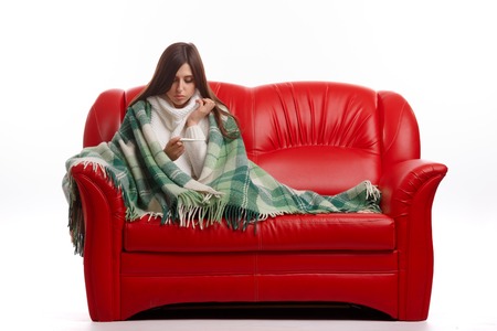 Young sick woman in scarf and pajamas looking at thermometer. Sick girl with a thermometer on a white background, isolate, flu, coldsの写真素材