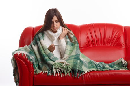 Young sick woman in scarf and pajamas looking at thermometer. Sick girl with a thermometer on a white background, isolate, flu, coldsの写真素材