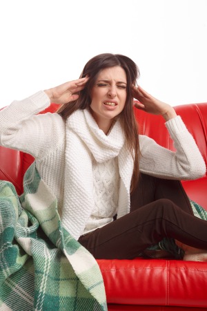 Sick young woman sitting on a couch and holding his head. Flu. Woman Caught Cold. Headache. Virus .の写真素材