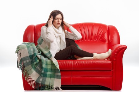 Sick young woman sitting on a couch and holding his head. Flu. Woman Caught Cold. Headache. Virus .の写真素材