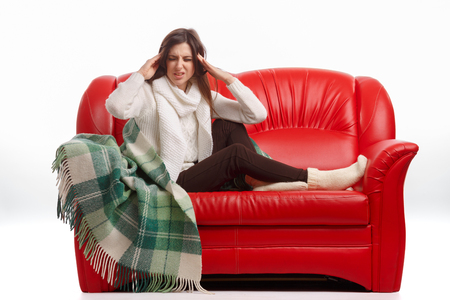 Sick young woman sitting on a couch and holding his head. Flu. Woman Caught Cold. Headache. Virus .の写真素材