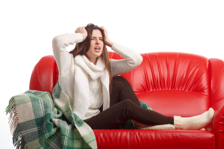 Sick young woman sitting on a couch and holding his head. Flu. Woman Caught Cold. Headache. Virus .の写真素材