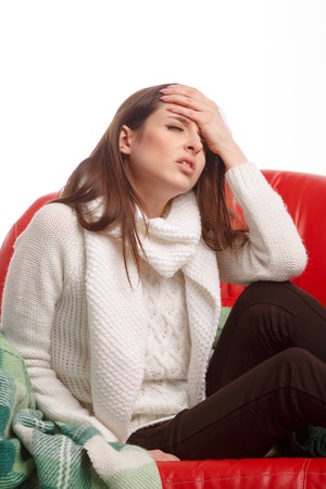 Sick young woman sitting on a couch and holding his head. Flu. Woman Caught Cold. Headache. Virus .の写真素材