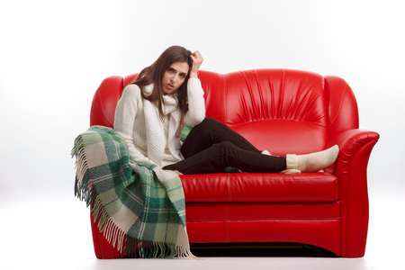 Sick young woman sitting on a couch and holding his head. Flu. Woman Caught Cold. Headache. Virus .の写真素材