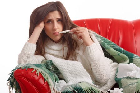 Young sick woman in scarf and pajamas looking at thermometer. Sick girl with a thermometer on a white background, isolate, flu, coldsの写真素材