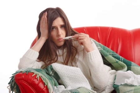 Young sick woman in scarf and pajamas looking at thermometer. Sick girl with a thermometer on a white background, isolate, flu, coldsの写真素材