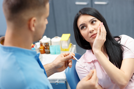 Girl patient goes to the dentist with a toothache in the dental office. Young woman holding the hand of a sick toothの写真素材