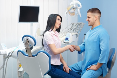 Young cheerful woman shaking hands with dentist in a dental clinic. People, medicine, stomatology and health care conceptの写真素材