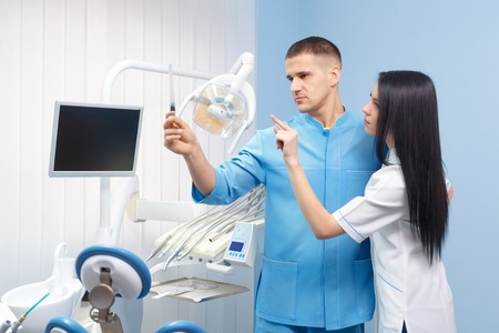 Male dentist and female assistant looking at x-ray picture in the dental office. People, medicine, stomatology and health care conceptの写真素材