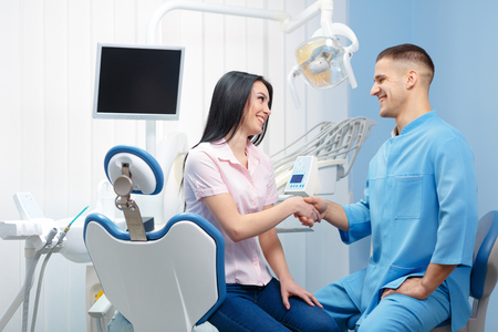 Young cheerful woman shaking hands with dentist in a dental clinic. People, medicine, stomatology and health care conceptの写真素材