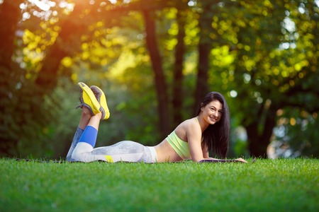 Young smiling woman doing fitness exercises in the park on the green grass. Fitness training in the sunlight.の写真素材