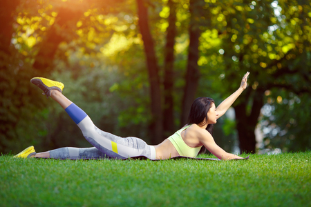 Young smiling woman doing fitness exercises in the park on the green grass. Fitness training in the sunlight.の写真素材