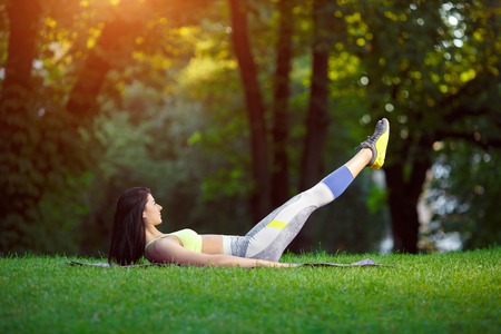 Young smiling woman doing fitness exercises in the park on the green grass. Fitness training in the sunlight.の写真素材