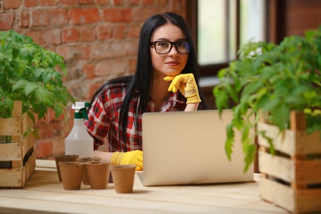 Staying connected. Portrait of a young beautiful gardener sitting using a laptop looking to the camera smiling.の写真素材