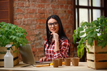 Effortless. Charming female wearing glasses sitting in front of a laptop in a greenhouse.の写真素材