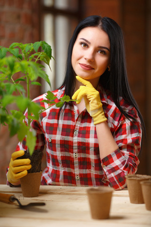 Healthy hobby. Portrait of a beautiful female holding a seedling and a pot in her hands looking to the camera smiling joyfully.の写真素材