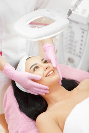 Beautiful woman receiving a facial massage in a beauty salon. The procedure of facial massage in beauty salon. Face Skin Care. Lifting Procedure. Beauty Concept. Spa Salon. Spa Face Massage.の写真素材
