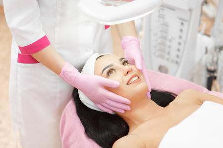 Beautiful woman receiving a facial massage in a beauty salon. The procedure of facial massage in beauty salon. Face Skin Care. Lifting Procedure. Beauty Concept. Spa Salon. Spa Face Massage.の写真素材