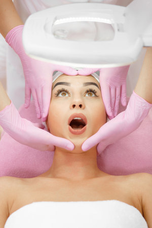 Surprised woman receiving a facial massage in a beauty salon. Face Skin Care. Lifting Procedure....