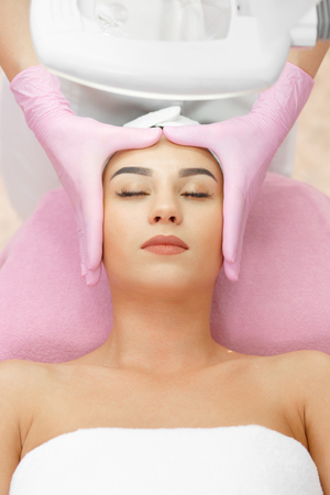 Face Lifting. Young woman getting facial massage in the cosmetology salon. Procedure of facial massage in cosmetology. Face Skin Care. Lifting Procedure. Cosmetology Salon. Cosmetology Face Massage.の写真素材