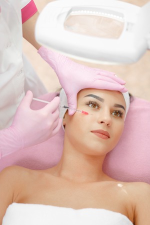 Woman gets injection in her face. Beauty woman giving botox injections. Young woman gets beauty facial injections in the cosmetology salon. Face aging injection. Aesthetic Medicine, Cosmetologyの写真素材