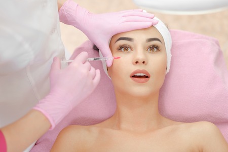 Woman gets injection in her face. Beauty woman giving botox injections. Young woman gets beauty facial injections in the cosmetology salon. Face aging injection. Aesthetic Medicine, Cosmetologyの写真素材