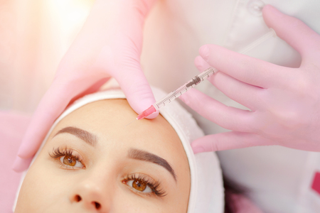 Woman gets injection in her face. Beauty woman giving botox injections. Young woman gets beauty facial injections in the cosmetology salon. Face aging injection. Aesthetic Medicine, Cosmetologyの写真素材